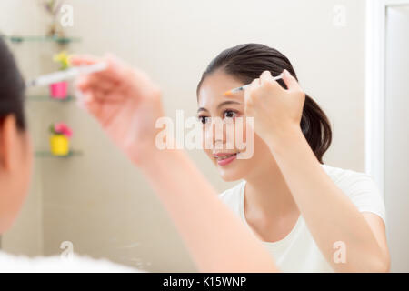 smiling beautiful woman looking at mirror reflection image using syringe injection beauty care medicine in forehead standing on bathroom at home. Stock Photo