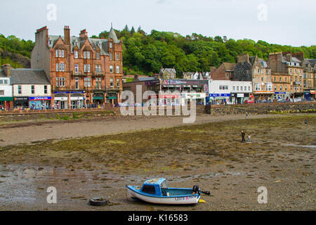 Scottish town of Oban with row of waterfront buildings with boat  in harbour at low tide in foreground Stock Photo