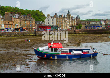 Scottish town of Oban with row of waterfront buildings with boat  in harbour at low tide in foreground Stock Photo