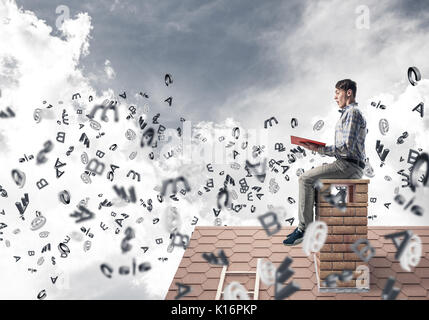 Man on brick roof reading book and symbols flying around Stock Photo