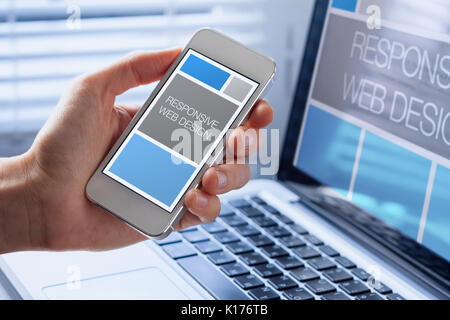 Designer sketching responsive web design website, close-up of hand with mobile phone screen showing fluid grid template with laptop computer in backgr Stock Photo
