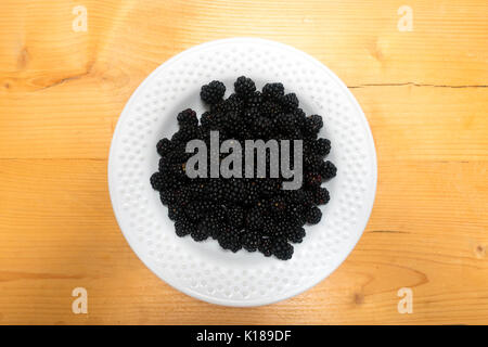 A white bowl of fresh hand picked blackberries from a UK hedgerow placed on a kitchen table with natural light, fruit in bowl Stock Photo