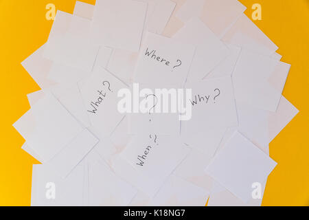 White square sheets of paper with questions spread out in chaotic order on a yellow background. Main questions. Stock Photo