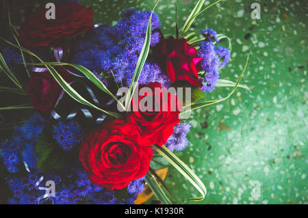 red roses with blue flowers in the bouquet on the background of green marble. Celebratory interior. Empty place for text. For this photo applied tonin Stock Photo