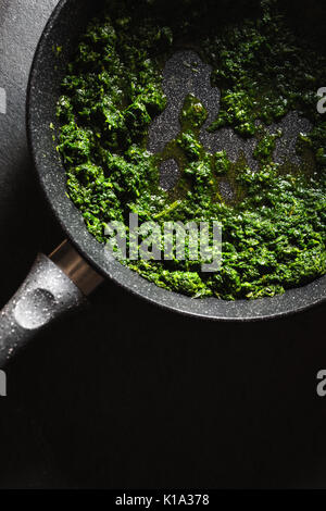 Roasting the chopped spinach leaves in a frying pan vertical Stock Photo