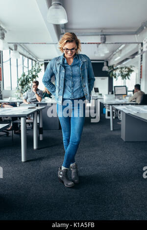 Businesswoman standing in office and looking down. Female business executive standing with crossed legs. Stock Photo