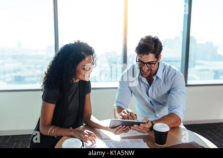 Smiling businessman and businesswoman in a discussion sitting at  a table in office. business colleagues using a tablet pc while discussing business f Stock Photo