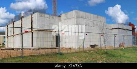 Behind the iron mesh fence is a concrete box of a newly constructed no name building. Panoramic summer collage from several photos Stock Photo