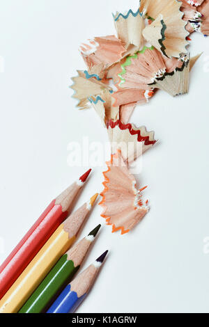 high-angle shot of a pile of pencil crayons of different colors and a pile of fan-shaped shavings of different colors on an off-white background Stock Photo