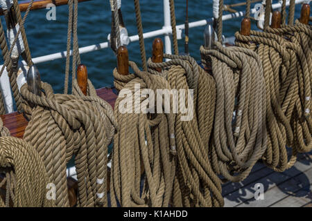 Detail shot of ropes and pulleys on a wooden schooner under sail, with blue water in the background Stock Photo