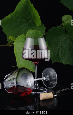 Two glasses of red wine on black backdrop with fresh vine leaves. Still life. Cork and opener. Vintage leaves on the background Stock Photo
