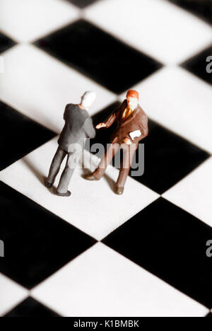 close up of two businessmen miniature figurines shaking hands on a chessboard Stock Photo