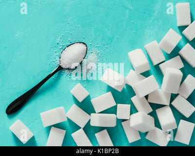 background of sugar cubes and sugar in spoon. White sugar on turquoise background. Sugar with copy space. Top view or flat lay Stock Photo