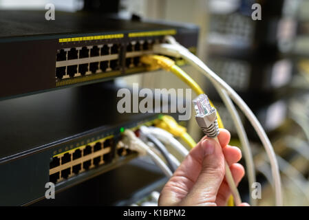 Hand with rj45 cable and network equipment on background Stock Photo