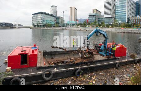 Rubbish collection boat on the Manchester Ship canal; HIAB on a barge collecting discarded plastic debris, rubbish, litter,  polluted, pollution, polystyrene, and toxic trash being removed from the banks of the canals in Salford Quays and Trafford, Greater Manchester, England. UK Stock Photo