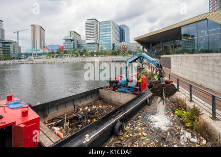 Rubbish collection boat on the Manchester Ship canal; HIAB on a barge collecting discarded plastic debris, rubbish, litter,  polluted, pollution, polystyrene, and toxic trash being removed from the banks of the canals in Salford Quays and Trafford, Greater Manchester, England. UK Stock Photo