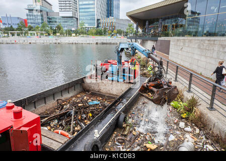 Rubbish collection boat on the Manchester Ship canal; HIAB on a barge collecting discarded plastic debris, rubbish, litter,  polluted, pollution, polystyrene, and toxic trash being removed from the banks of the canals in Salford Quays and Trafford, Greater Manchester, England. UK Stock Photo