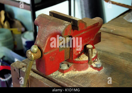 A red rustic vice clamp sitting on a workbench covered with wood dust. Stock Photo