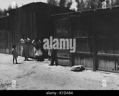 Mexican family, with women and girls, standing on a dirt road, between two wooden farm buildings, California, 1935. From the New York Public Library. Stock Photo