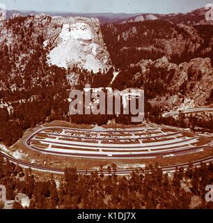 A photograph of Mount Rushmore, taken from a great distance, vantage point was level with the top of the monument, roads leading in and out of the park, along with the parking lot can be seen in the foreground, in the Black Hills in Keystone, South Dakota, 1975. Stock Photo