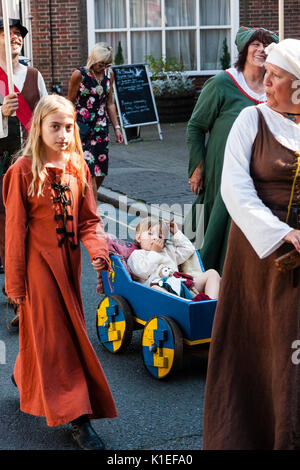 England, Sandwich. Medieval living history family walking past with young boy asleep in little hand cart. Stock Photo