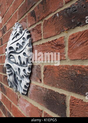 Sun god garden ornament on a red brick wall, UK Stock Photo