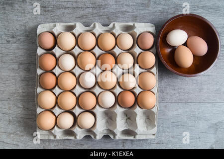 Carton of brown eggs with three selected in a wooden bowl Stock Photo