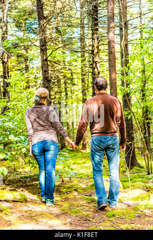 Back of young couple holding hands walking through fairy tale forest with mossy ground in West Virginia Stock Photo