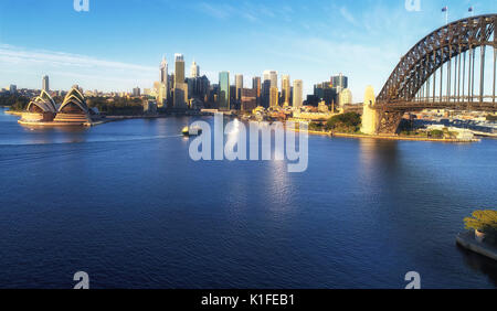 Panorama of Sydney City CBD and Ferry to Manly in view of Circular Quay wharfs, high-rise busienss towers and Sydney Harbour bridge around Harbour. Stock Photo