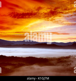 Dawn in mountains covered mist. Bright orange sky. Stock Photo