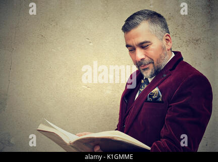 Mature man reading an old book standing by a concrete wall outdoors Stock Photo
