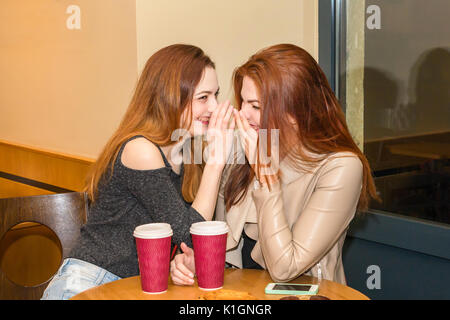 Two beautiful women drinking coffee mug, gossiping and chatting in a cafe bar. Two girls sitting in a cafeteria, gossiping and laughing Stock Photo