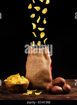 Potato chips fall into a canvas bag isolated on a black background. Flying chips closeup. Stock Photo