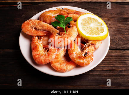 Prepared shrimp with lemon and parsley on a white plate on wooden background