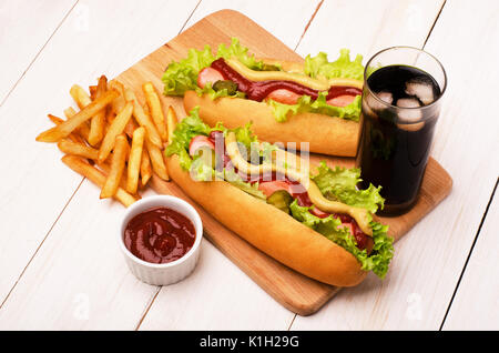 Grilled hot dogs with mustard, ketchup with glass of cola and french fries on a picnic table Stock Photo