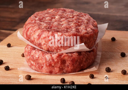 Raw burger cutlet with black pepper on black wooden background Stock Photo