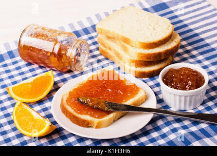 Jar of orange jam with bread on checkered blue tablecloth, closeup Stock Photo