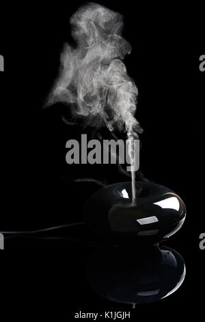 Black plastic aroma diffuser with streaming smoke on black reflecting background Stock Photo