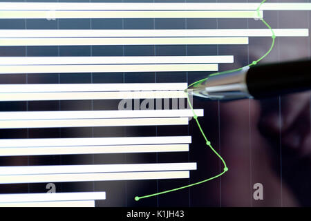 Analyzing stock market from a digital computer screen over a detailed diagram. Pointing out some details with a pen. Stock Photo