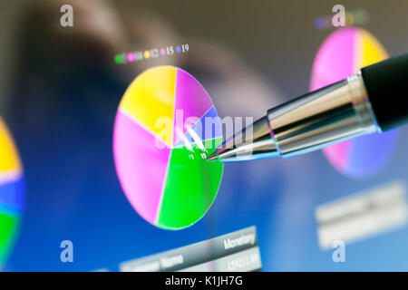 Analyzing stock market from a digital computer screen over a detailed diagram. Pointing out some details with a pen. Stock Photo