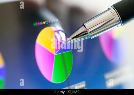 Analyzing stock market from a digital computer screen over a detailed diagram. Pointing out some details with a pen. Stock Photo