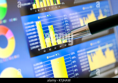 Analyzing stock market from a digital computer screen over a detailed diagram. Pointing out some details with a pen. Stock Photo