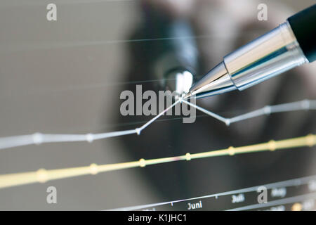Analyzing stock market from a digital computer screen over a detailed diagram. Pointing out some details with a pen. Stock Photo