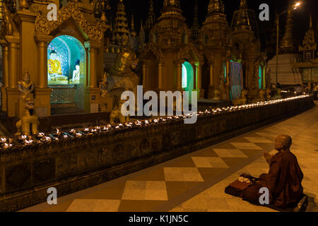 Buddhist monk prays in front of Buddha image in Shwedagon Pagoda, Yangon, Myanmar. Stock Photo