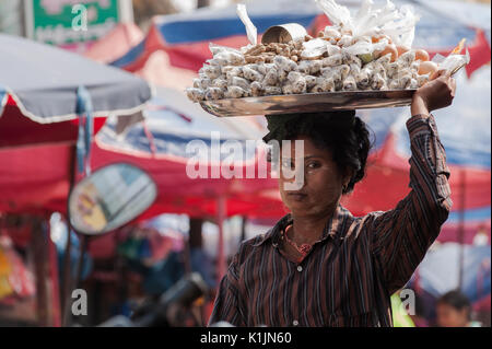 A woman sells snacks carried on top of her head at Central Market in Mawlamyine, Mon State, Myanmar. Stock Photo