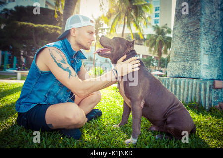 Man and dog american pit bull terrier relaxing at the park embracing and hugging Stock Photo