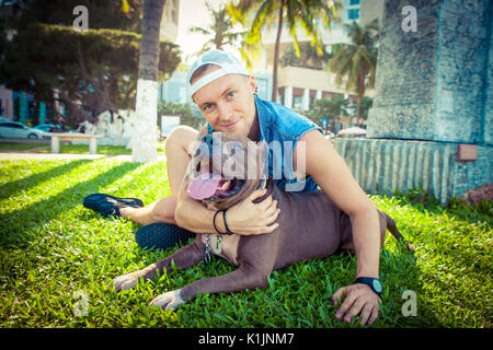 Man and dog american pit bull terrier relaxing at the park embracing and hugging Stock Photo