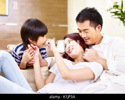 young asian mother and father sitting on couch at home having fun playing with son. Stock Photo