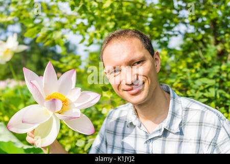 Portrait closeup of young man smiling holding bright white and pink lotus flower with yellow seedpod inside Stock Photo