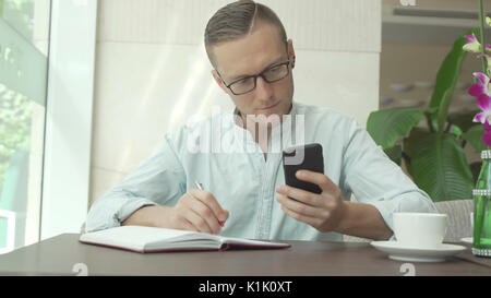 Businessman writing in daily planner and check notes on smartphone Stock Photo